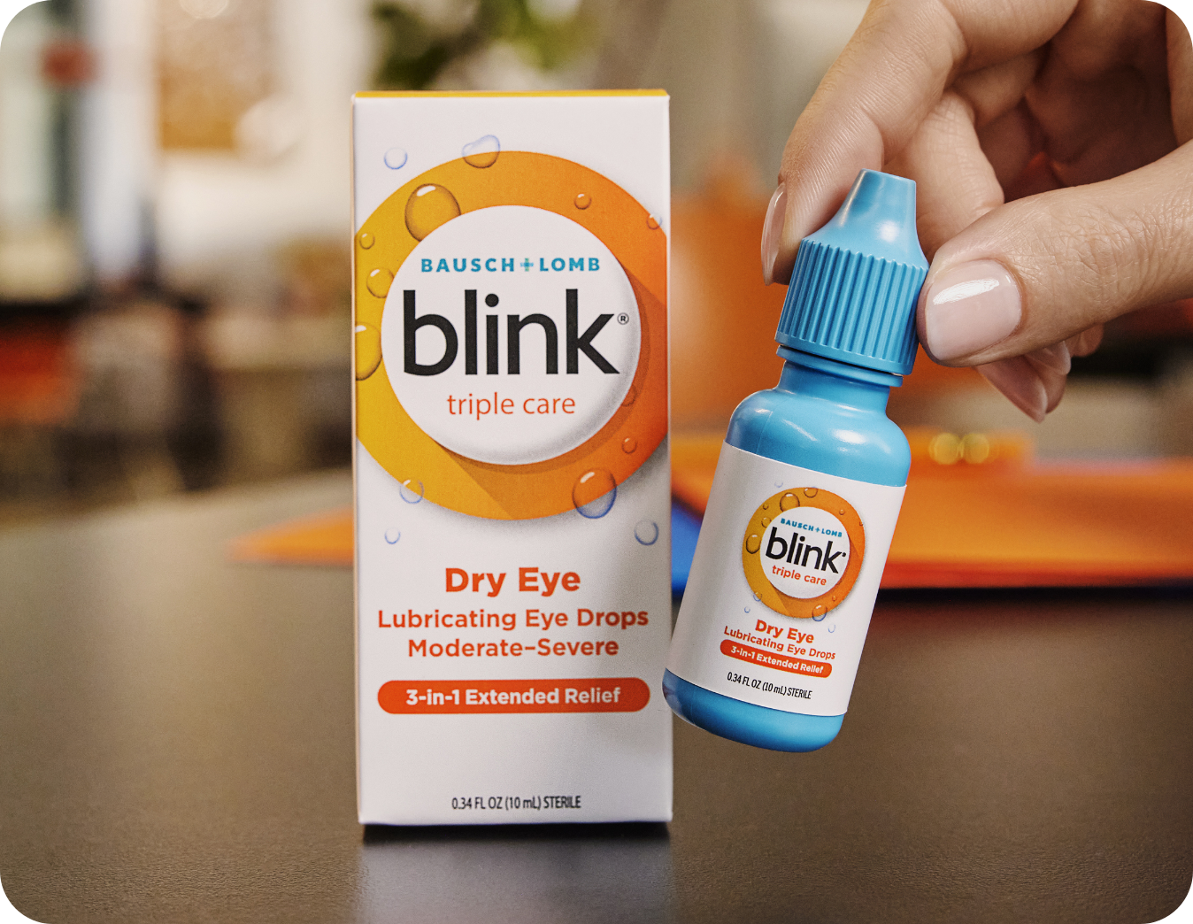Blink Triple Care eye drops packaging next to a hand holding the bottle.