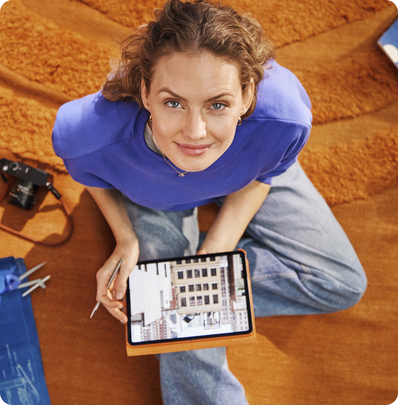 Woman sitting on a rug holding a tablet looking up 