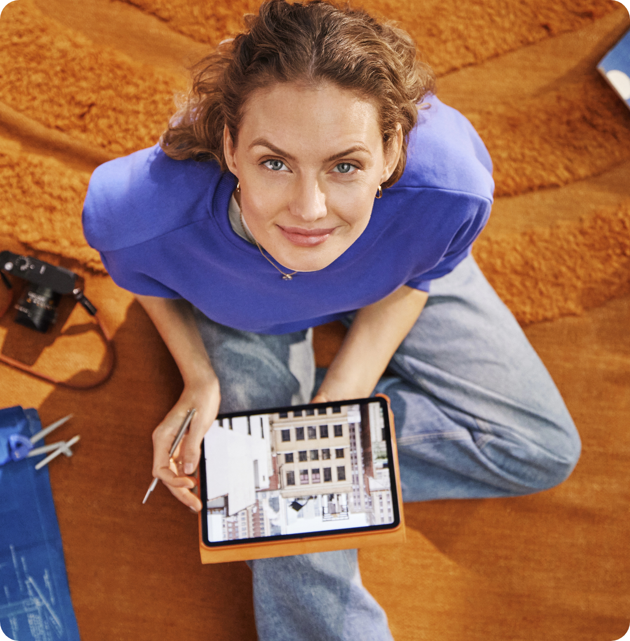 Woman sitting on a rug holding a tablet looking up 